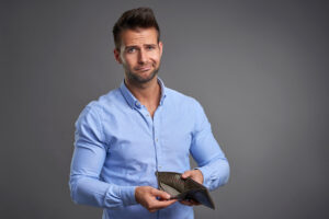 Los Angeles buy here pay here car dealership - A poor handsome young man feeling stressed looking in to the camera and showing his empty wallet.